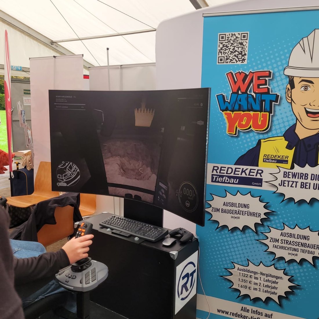 Baggersimulator neben dem Roll-up mit den Ausbildungsberufen Baugeräteführer und Straßenbauer