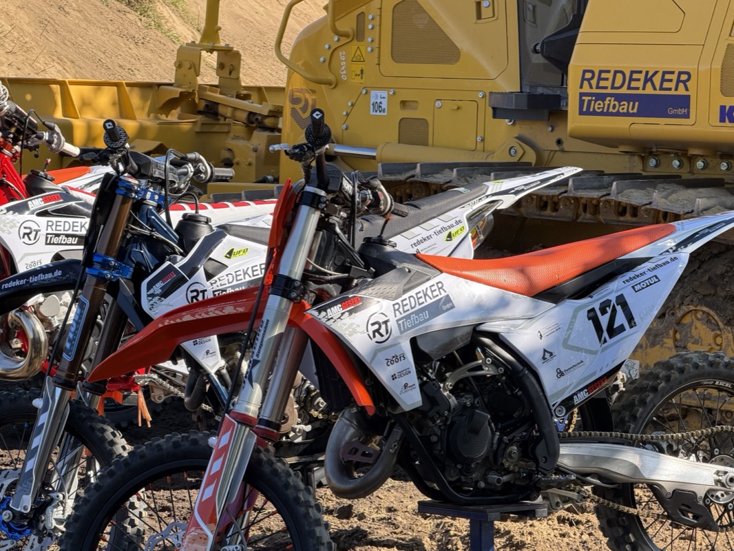 Motocross-Motorrad im Redeker-Tiefbau-Design vor einem Baggerlader der Redeker Tiefbau GmbH