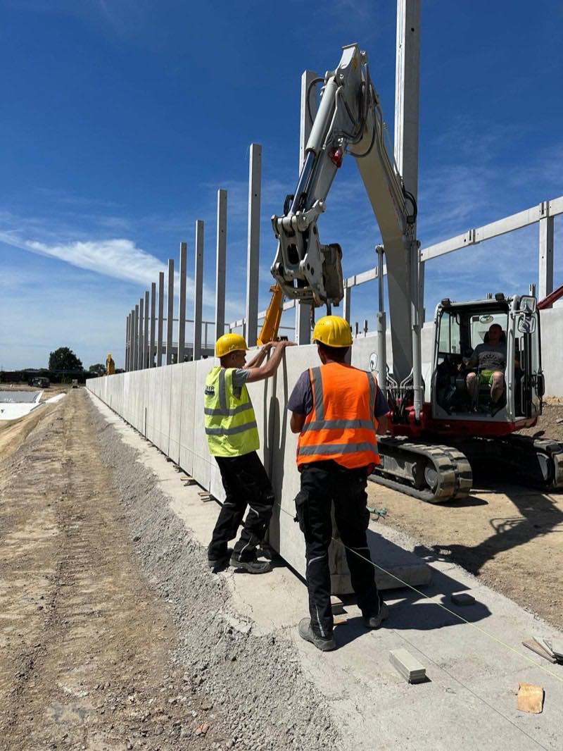 Zwei Bauarbeiter richten mit dem Bagger ein Betonfertigteil aus