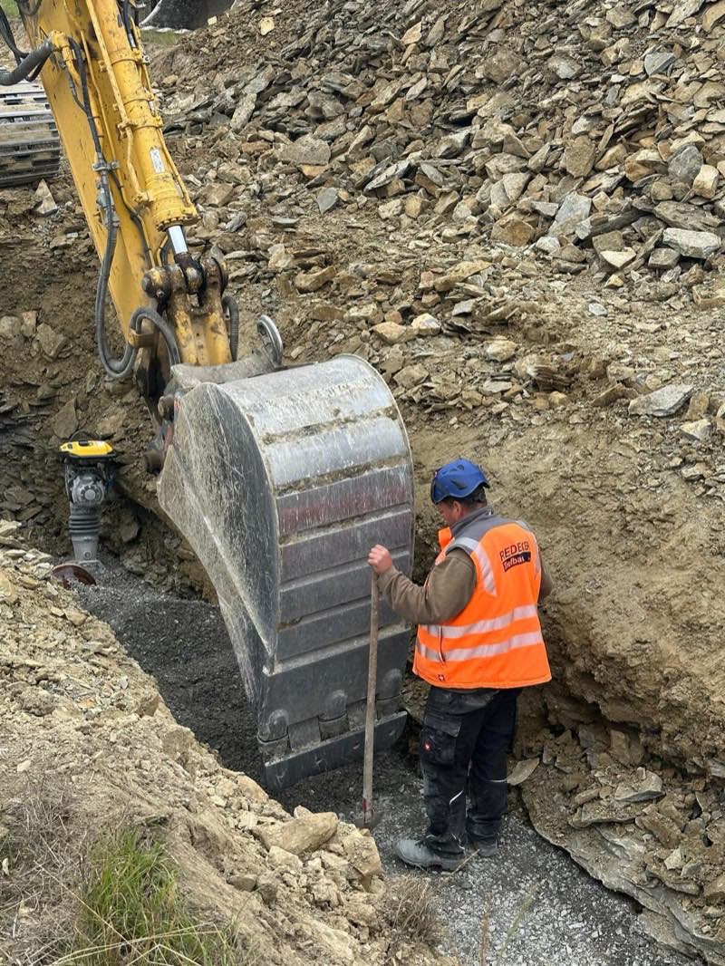 Kanalbauer prüft die Grabensohle neben der Baggerschaufel