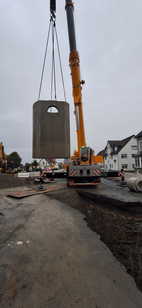 Autokran hebt einen Betonschacht in eine aufgegrabene Straße
