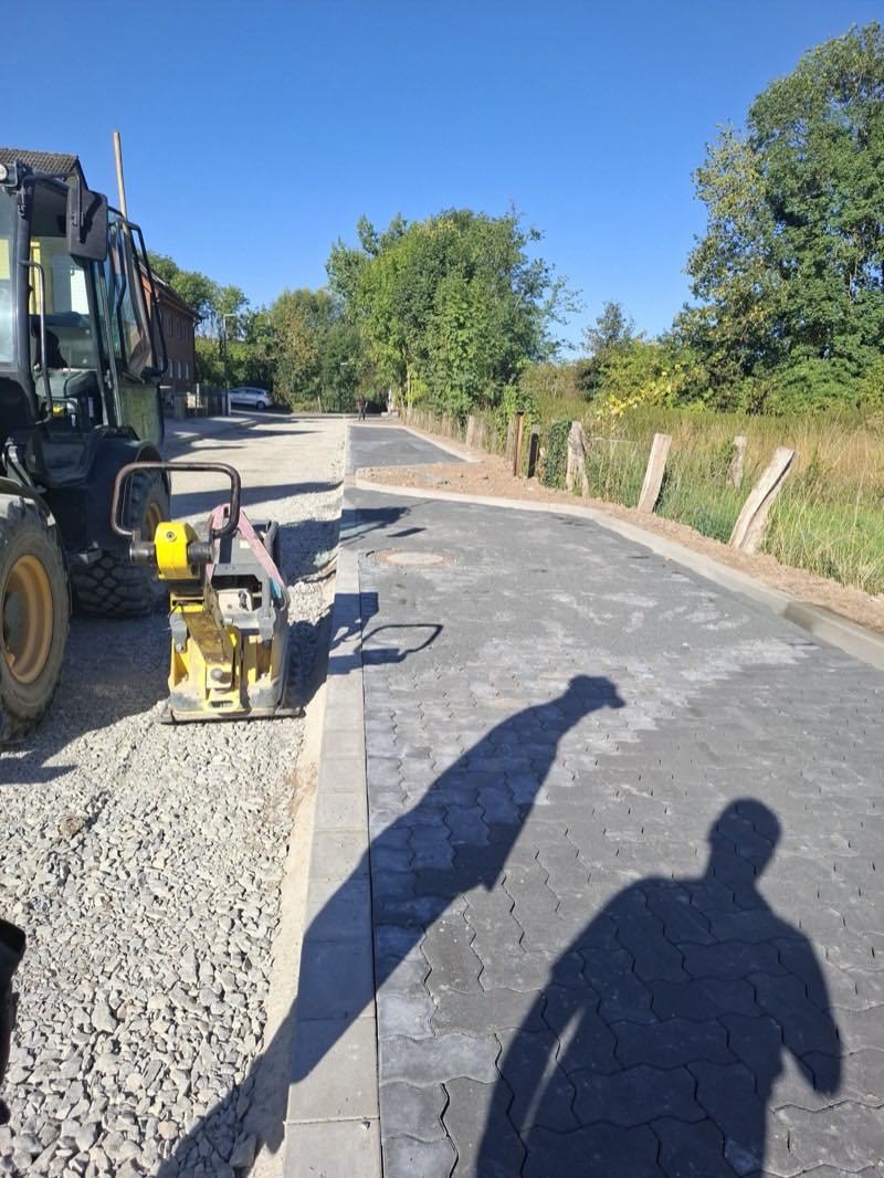 Rüttelplatte und Radlader auf einem frisch gepflasterten Wirtschaftsweg