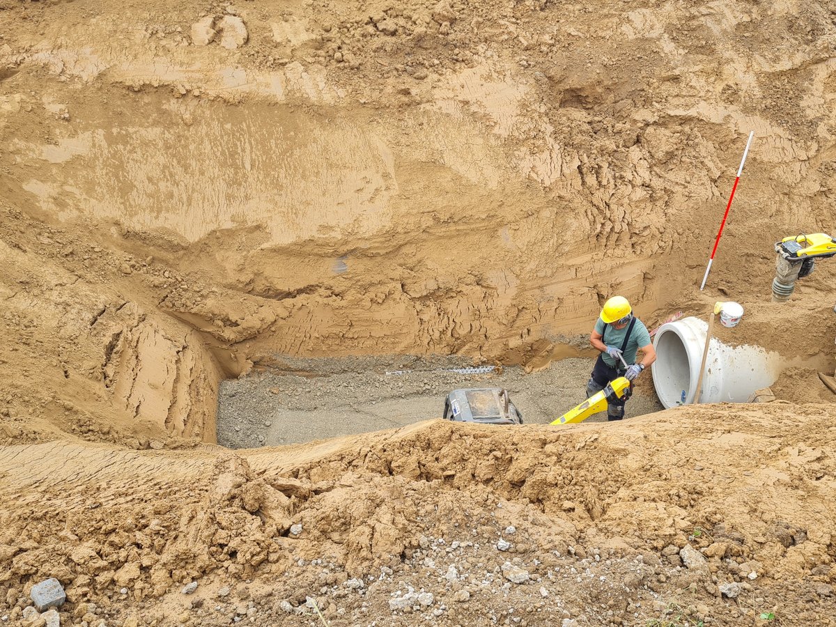 Kanalbauer setzt ein Betonrohr in der Baugrube an