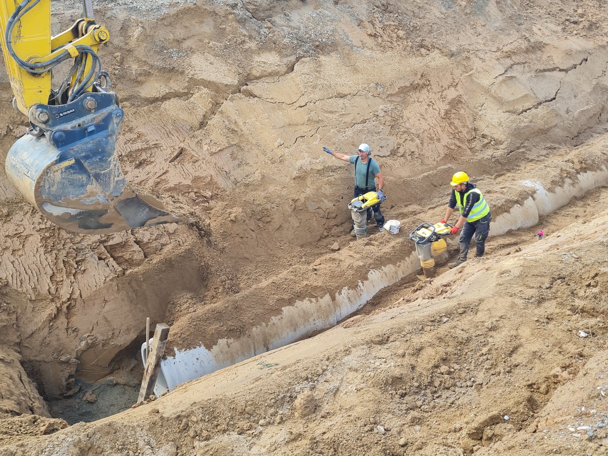 Zwei Kanalbauer verdichten die Grabensohle über der Rohrleitung